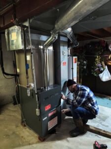 An HVAC technician servicing a Goodman furnace and ductwork in a basement for Dad's Heating and Cooling in Blue Springs, MO.