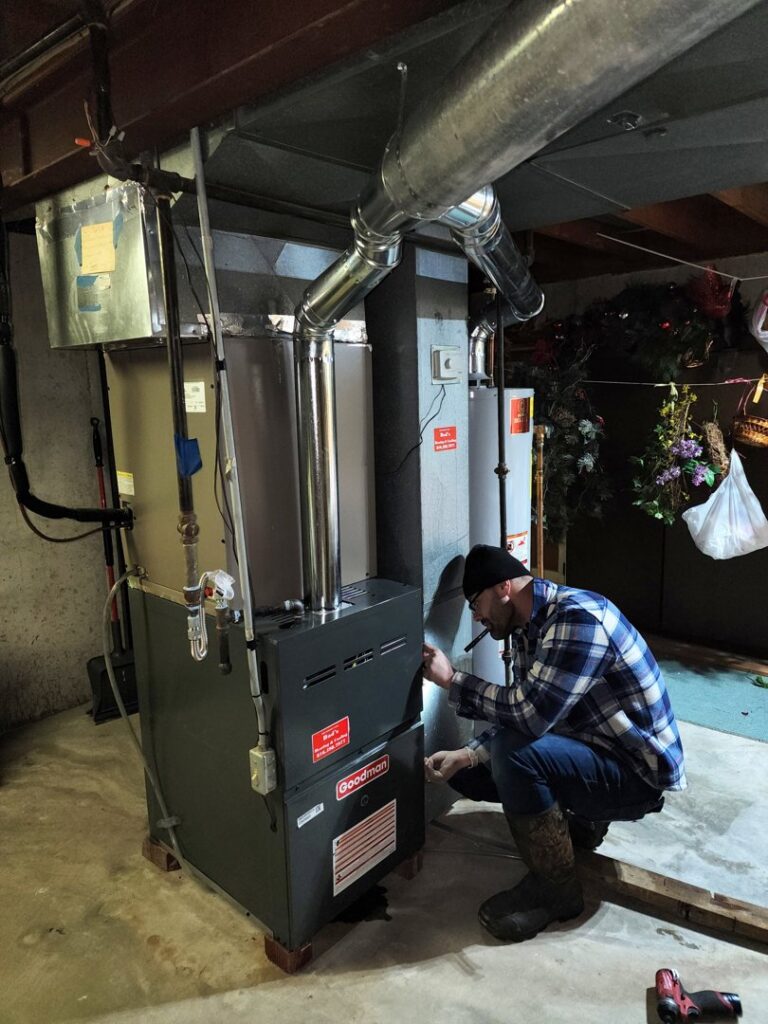 An HVAC technician servicing a Goodman furnace and ductwork in a basement for Dad's Heating and Cooling in Blue Springs, MO.