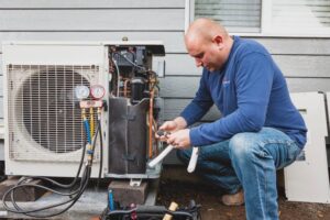 An HVAC technician servicing an outdoor heat pump unit with gauges and tools at The Heat Pump Store in Portland, OR.