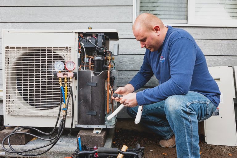 An HVAC technician servicing an outdoor heat pump unit with gauges and tools at The Heat Pump Store in Portland, OR.
