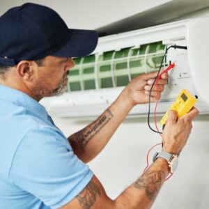 An HVAC technician servicing an indoor split air conditioning unit with a multimeter for Reliance Home Comfort, LLC in Hampton, VA.