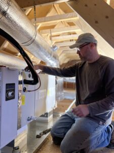 An HVAC technician servicing an indoor air handler or furnace unit in an attic space for HVAC Fellows in Boston, MA.
