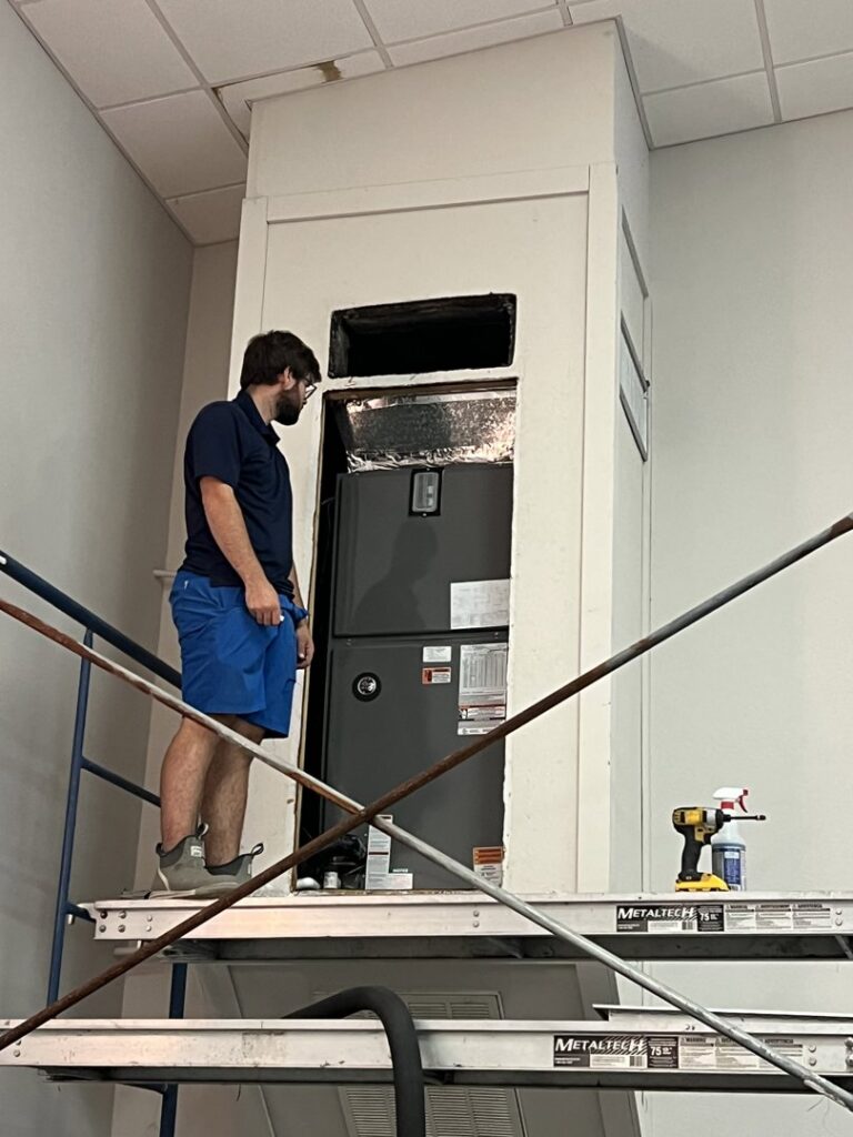 An HVAC technician on scaffolding servicing an indoor air handler unit for Moreau's Heating & AC in Lake Charles, LA.