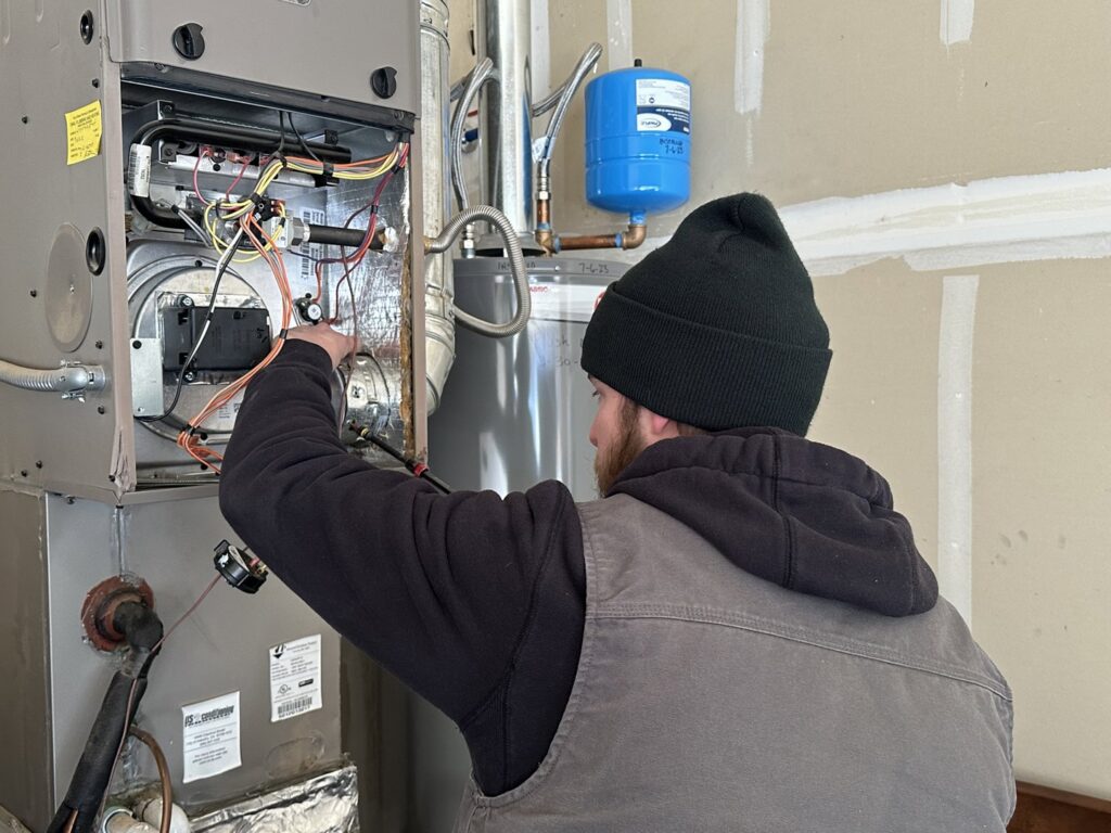 An HVAC technician servicing an indoor furnace unit for Access Heating & Air Conditioning in Fredericksburg, VA