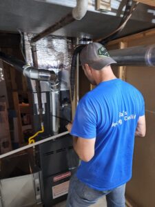 An HVAC technician servicing an indoor furnace and ductwork, wearing a Dad's Heating & Cooling shirt in Blue Springs, MO.