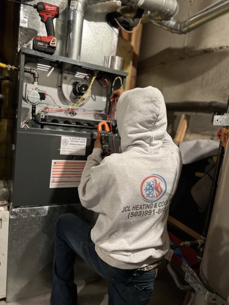 An HVAC technician from JCL Heating and Cooling LLC servicing an indoor furnace unit in Gresham, OR.