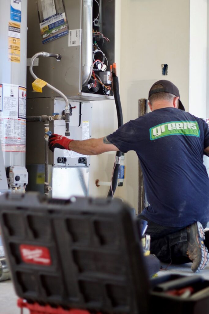An HVAC technician from Greens Heating & Air Conditioning servicing an indoor HVAC unit and water heater, Douglasville, GA.