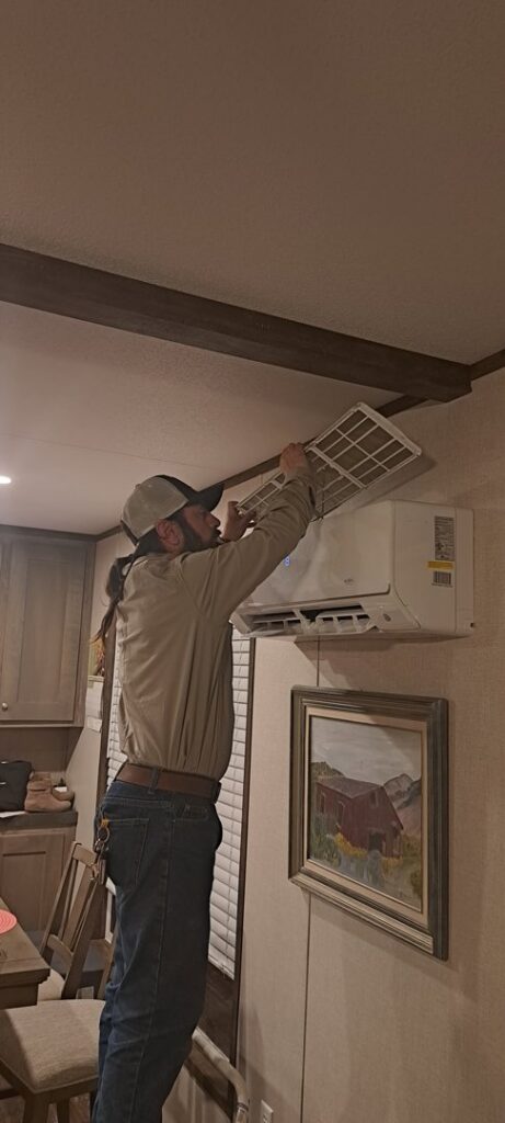 An HVAC technician servicing a wall-mounted mini-split AC unit for Desert Sage Heating and Cooling in Albuquerque, NM.