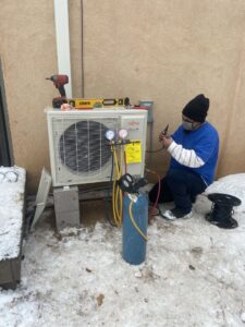 An HVAC technician servicing an outdoor Fujitsu mini-split condenser unit with gauges and tools in the snow for Santa Fe Heating & Cooling LLC in Santa Fe, NM.
