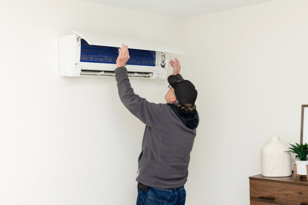 An HVAC technician servicing a wall-mounted mini-split unit for a client of Warren Mechanical, LLC in Carmel, IN.