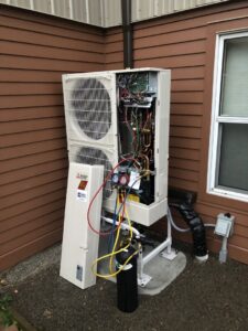 An HVAC technician servicing an outdoor Mitsubishi Electric unit with its panel open and gauges connected, by Simply Installs Heating & Air Conditioning in Shortsville, NY.
