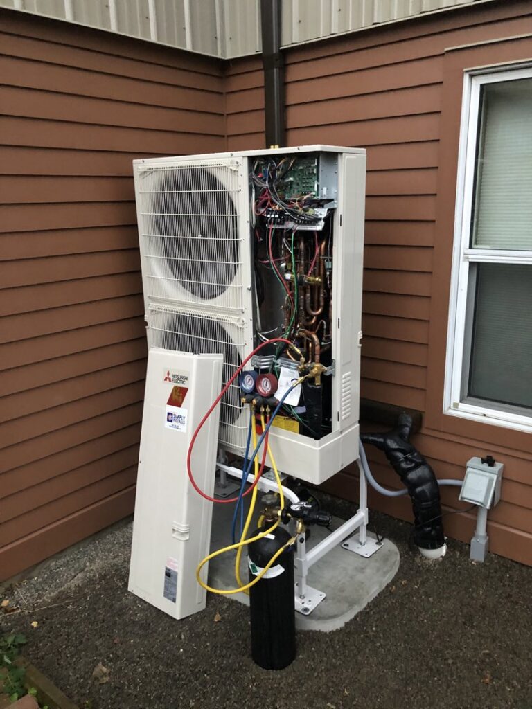 An HVAC technician servicing an outdoor Mitsubishi Electric unit with its panel open and gauges connected, by Simply Installs Heating & Air Conditioning in Shortsville, NY.