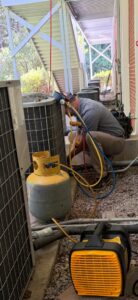 An Icy Hot Heating and Air Conditioning technician servicing multiple outdoor AC units in Raleigh, NC.