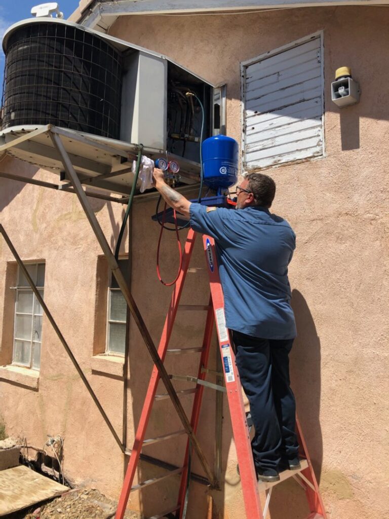 An HVAC technician from Ace A/C & Heating servicing an outdoor air conditioning unit on a ladder in Henderson, NV.