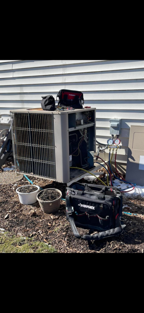 An HVAC technician servicing an outdoor air conditioning unit with tools and gauges, demonstrating work by ACW Heating & Air in North Aurora, IL