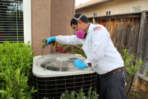 An HVAC technician servicing an outdoor air conditioning unit with a drill for Controlled Climates Heating and Air Conditioning, Inc. in Fresno, CA.