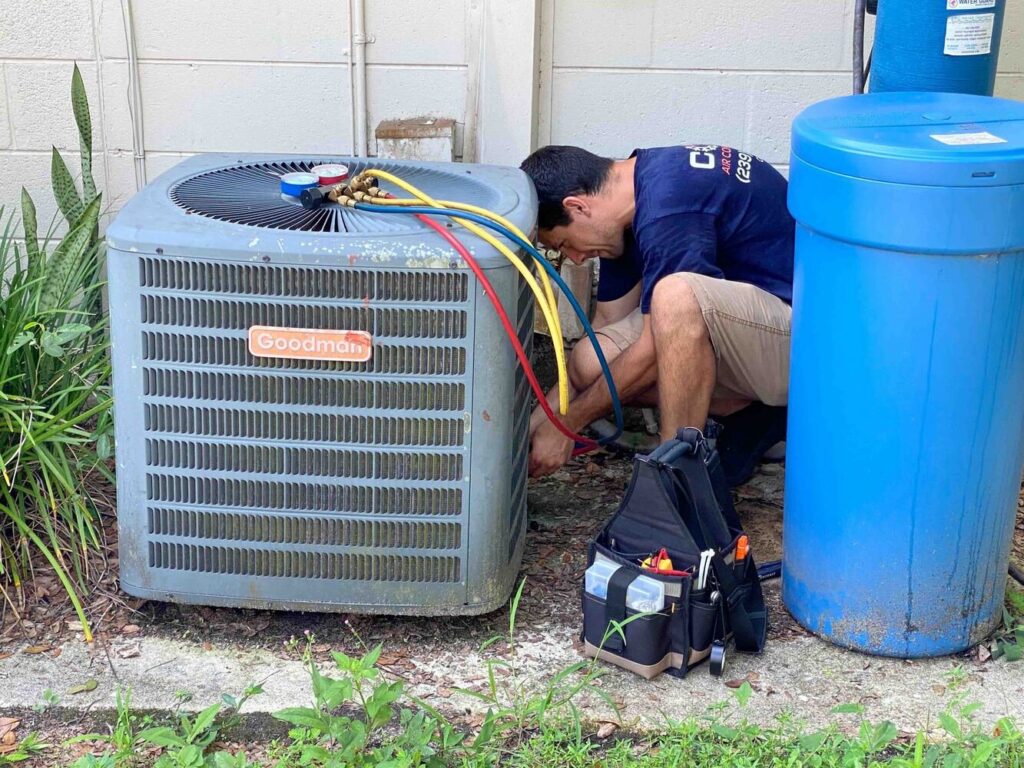 An HVAC technician from Coral Air Conditioning servicing an outdoor Goodman AC unit with gauges in Cape Coral, FL.