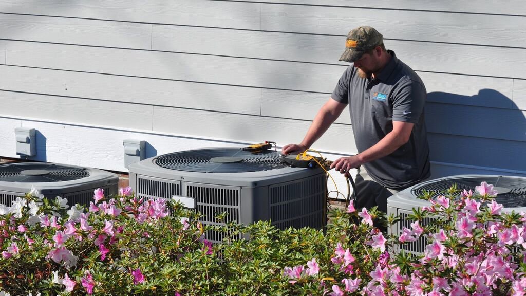 An HVAC technician servicing an outdoor air conditioning unit for Foust Heating & Air Conditioning in Fayetteville, NC.