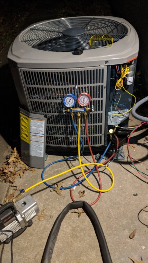 An HVAC technician servicing an outdoor air conditioning unit with gauges and a vacuum pump at Goodpaster's Mechanical, Inc. in Broken Arrow, OK.