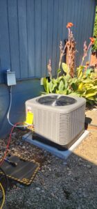 An HVAC technician from Nelke Mechanical servicing an outdoor air conditioning unit with tools and gauges in Keizer, OR.