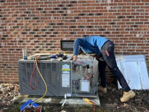 An HVAC technician servicing an outdoor air conditioning unit with tools for Oakes AC Services, LLC in Louisburg, NC