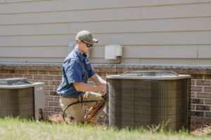 An HVAC technician kneeling and servicing an outdoor AC unit at On Call Plumbing, Heating & Air in Columbia, SC