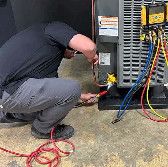 An HVAC technician connecting service hoses to an outdoor air conditioning unit during a maintenance call by Prime Home HVAC in York, PA.
