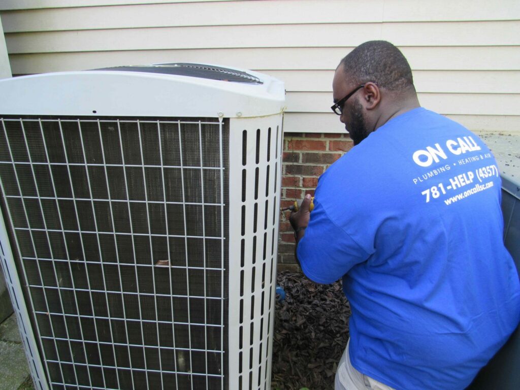 An HVAC technician servicing the side panel of an outdoor AC unit for On Call Plumbing, Heating & Air in Columbia, SC