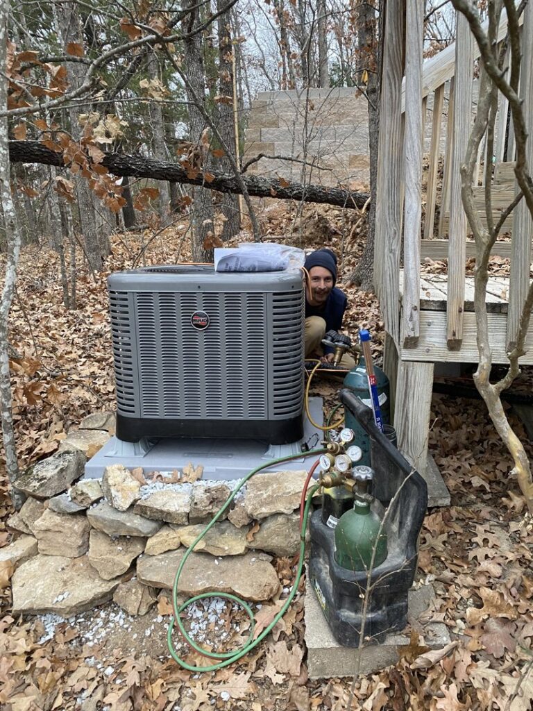 An HVAC technician servicing an outdoor AC unit with refrigerant tanks and gauges for Stanton Home Comfort in Fordland, MO.