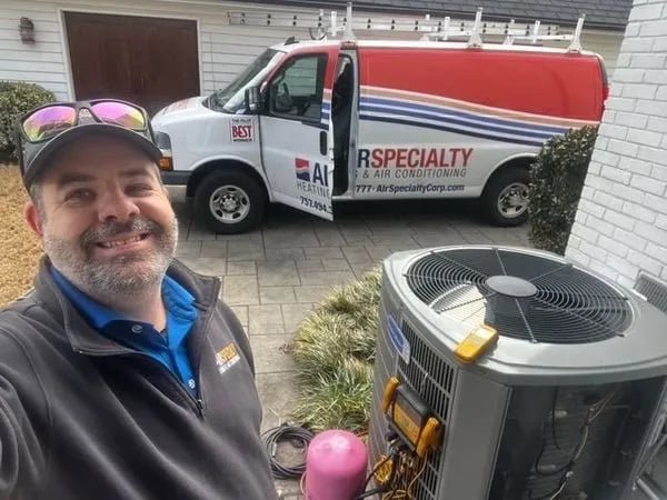 An Air Specialty Heating & Air Conditioning technician servicing an outdoor HVAC condenser unit in Norfolk, VA.