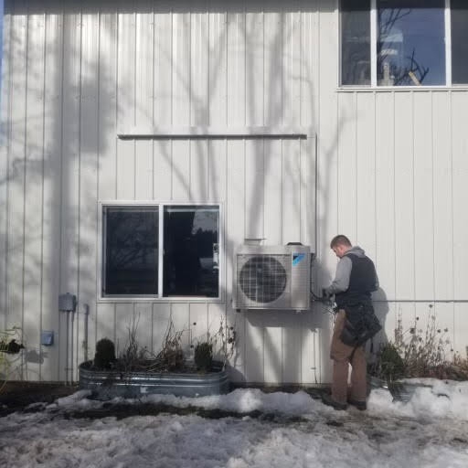 An HVAC technician servicing an outdoor mini-split unit on a building wall for AP HVAC in Ridgewood, NY.