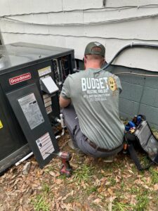 An HVAC technician from Budget Heating and Air servicing an outdoor condenser unit in Mobile, AL.