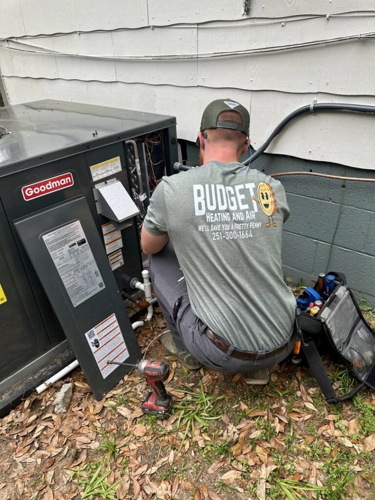 An HVAC technician from Budget Heating and Air servicing an outdoor condenser unit in Mobile, AL.