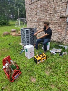 An HVAC technician servicing an outdoor condenser unit with tools on the grass for Gouker's Best Air in Franklin, TN.