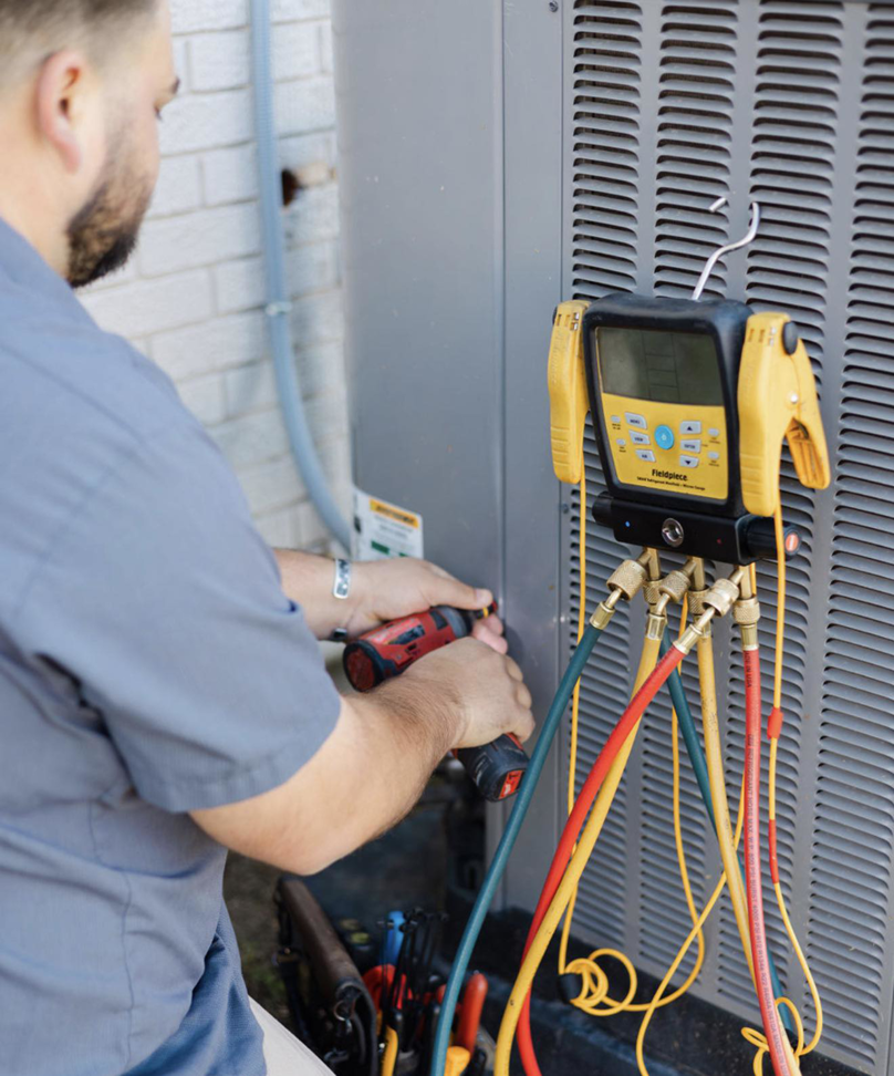An HVAC technician servicing an outdoor air conditioning unit with gauges at Target Temp, LLC in Houma, LA.