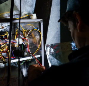 An HVAC technician from Triple-O servicing an outdoor air conditioning unit in Bergen, NY.
