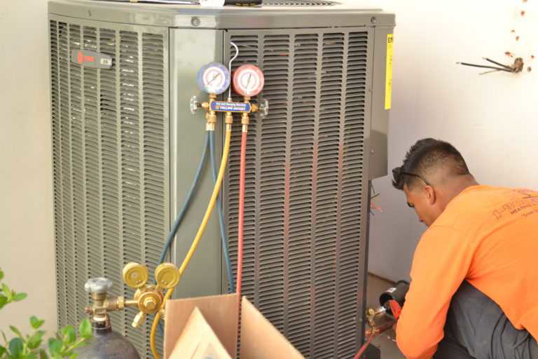 An HVAC technician connecting gauges to an outdoor air conditioning unit for service or repair by 1 800 Cooling, INC in Phoenix, AZ.