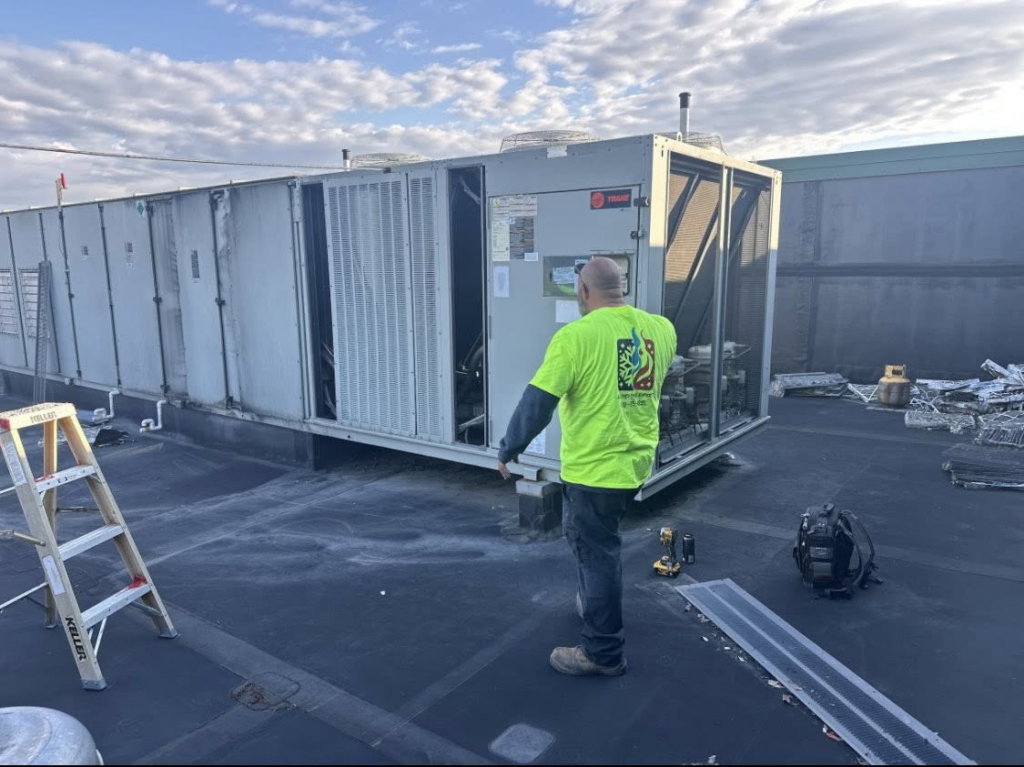 An HVAC technician servicing a large commercial rooftop system for Air Conditioning Experts in Orlando, FL.
