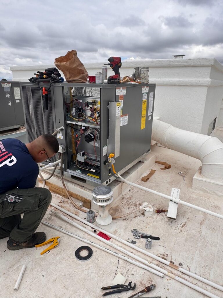 An HVAC technician servicing an open rooftop unit with tools on a commercial building for Anchor Air in El Paso, TX