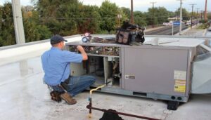An HVAC technician servicing a rooftop HVAC unit with gauges and tools for Energy Logix in Austin, TX.