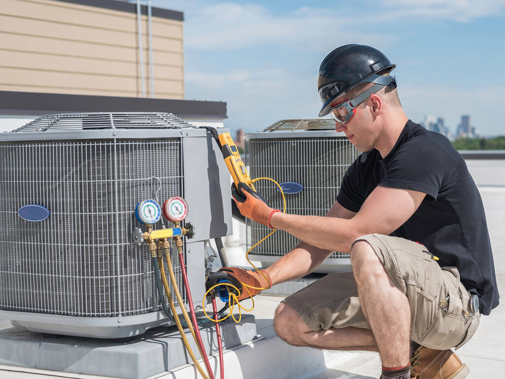 An HVAC technician servicing a rooftop air conditioning unit with gauges and tools for Garden City Plumbing & Heating in Missoula, MT