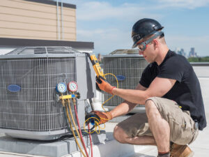 An HVAC technician servicing a rooftop air conditioning unit with gauges and tools for Garden City Plumbing & Heating in Missoula, MT