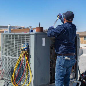 An HVAC technician connecting gauges to a rooftop air conditioning unit for service by EA Heating & Cooling in El Paso, TX.