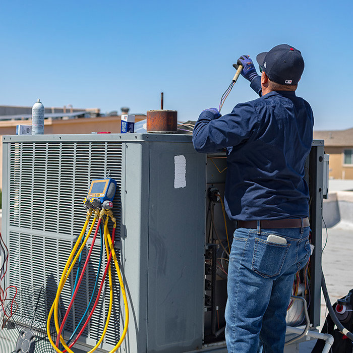 An HVAC technician connecting gauges to a rooftop air conditioning unit for service by EA Heating & Cooling in El Paso, TX.