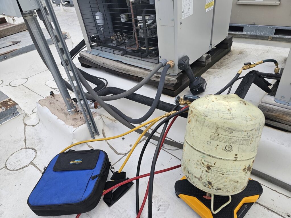 An HVAC technician servicing a commercial rooftop unit with gauges and a refrigerant tank for Henry Refrigeration & Hvac Utah in Ogden, UT.
