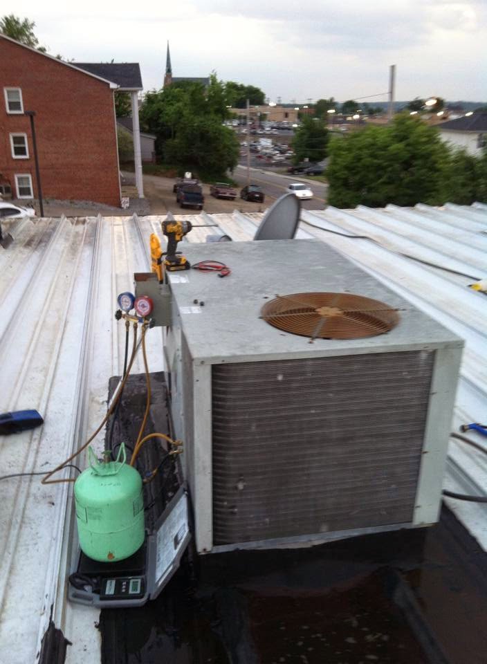 An HVAC technician servicing a rooftop unit with gauges and a refrigerant tank for Johnson's Heating and Cooling in Clarksville, TN.