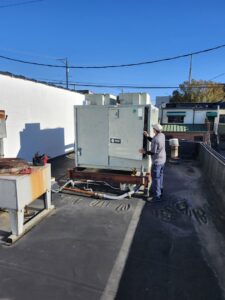 An HVAC technician from SBS-NC, LLC performing service on a large rooftop unit in High Point, NC.