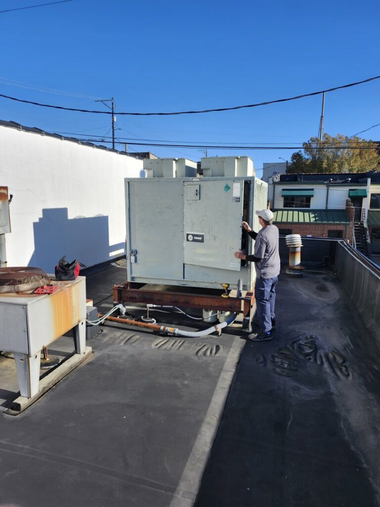 An HVAC technician from SBS-NC, LLC performing service on a large rooftop unit in High Point, NC.