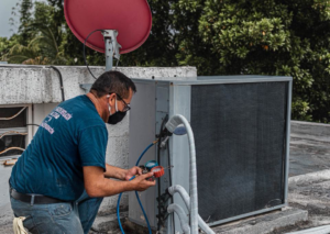 An HVAC technician servicing a rooftop air conditioning unit with gauges for TC A/C & Refrigeration in Lafayette, LA
