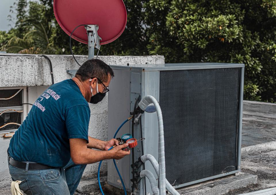 An HVAC technician servicing a rooftop air conditioning unit with gauges for TC A/C & Refrigeration in Lafayette, LA